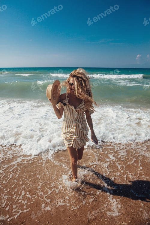 Preview: Smiling girl with blond curly hair running from sea waves