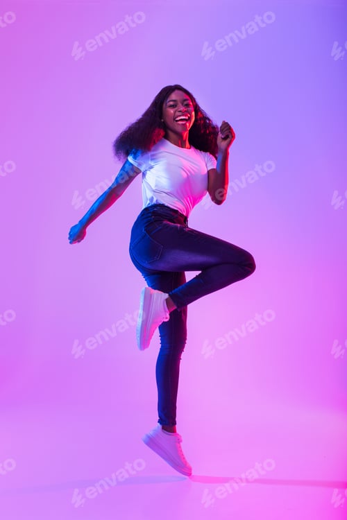 Preview: Joyful millennial African American woman flying in air, jumping, smiling at camera in neon light