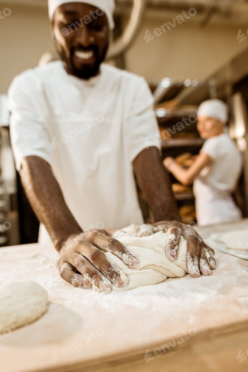 Preview: close-up shot of african american baker kneading dough at baking manufacture