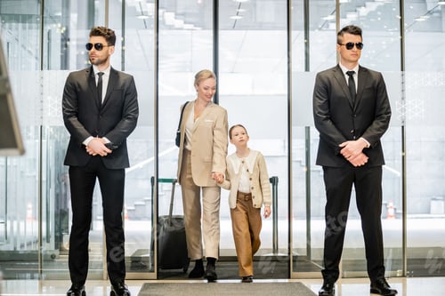 Preview: private security concept, two bodyguards in formal wear and sunglasses standing near hotel