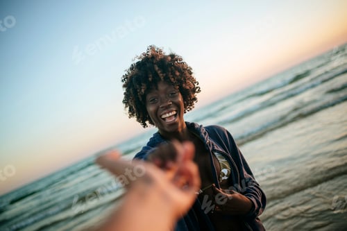 Preview: Cheerful woman leading someone by the hand at the beach during sunset