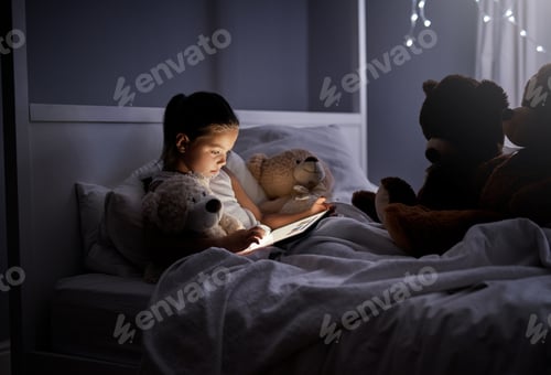 Preview: Shot of an adorable little girl using a digital tablet in bed at night