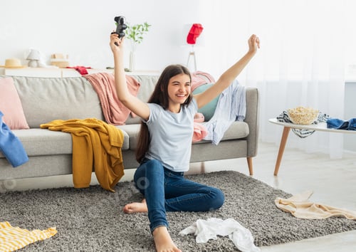 Preview: Indian teenage girl playing video games with joystick, sitting on floor and raising hands