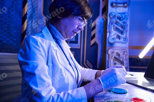 Preview: middle aged woman scientist in goggles working with alien life samples in petri dishes in lab