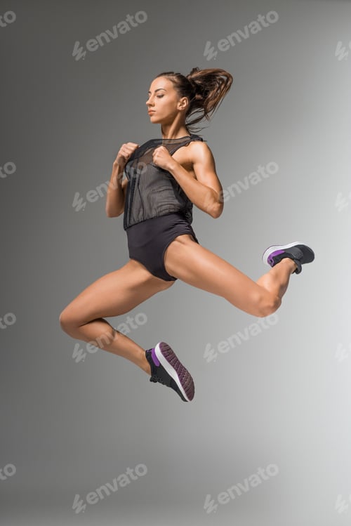 Preview: gorgeous young woman in sportswear and sneakers jumping isolated on grey