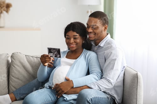 Preview: Smiling pregnant black couple holding ultrasound image, home interior