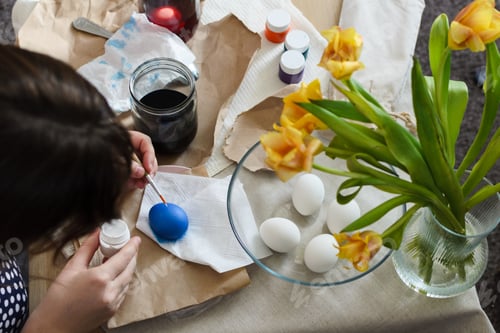 Preview: Top view of a table in a creative mess, on which a woman prepares for the Easter holiday, paints egg