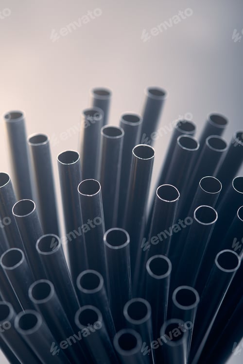 Preview: Bunch of black plastic straws scattered in container over plain grey background. Copy space for text