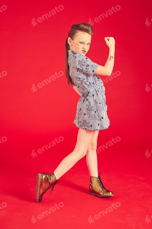 Preview: Confident young girl posing with a fist up on a red backdrop