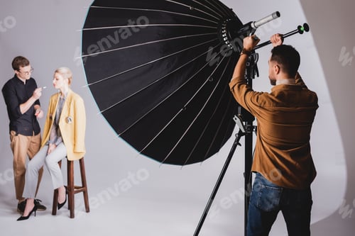 Preview: selective focus of photographer touching reflector on backstage and Makeup Artist doing makeup to
