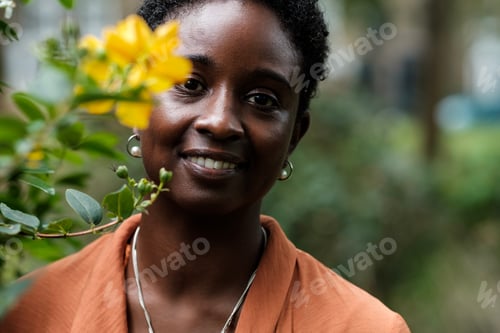 Preview: Smiling black woman looking at camera beside blurred flower.