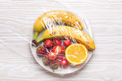Preview: Assorted different fruit and berries on white plate wrapped in plastic clear film top view on white