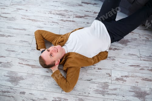 Preview: Happy young man lying on the floor near the sofa in the living room and resting