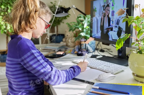 Preview: Girl child sitting at home at table with computer listening online lesson
