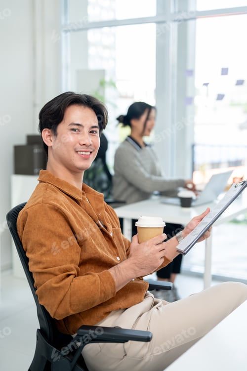 Preview: A handsome Asian businessman sits at his desk, smiling at the camera.