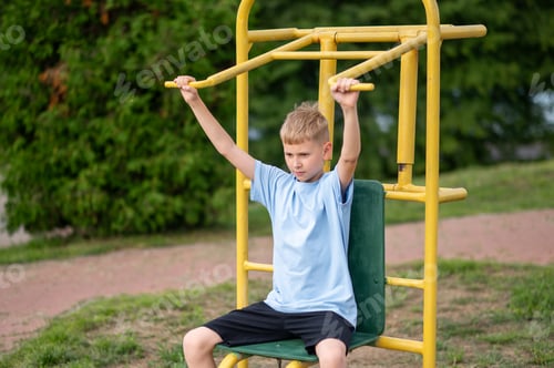 Preview: Teen boy training on outdoor fitness machine in summer park