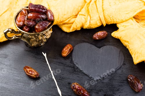 Preview: Dry fruit dates in golden cup near slate black heart. Copy space.Valentine Day.