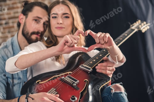 Preview: Young couple holding guitar and woman shows heart sign with fingers