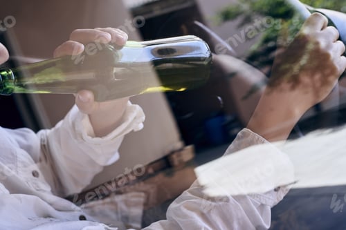 Preview: A woman driving a car while drinking beer from a bottle as seen through a car glass window.
