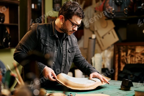 Preview: Portrait of leather craftsman makes a leather motorcycle seat at table in workshop studio