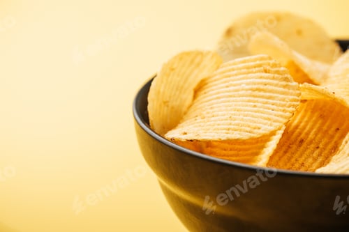 Preview: close up view of delicious crispy potato chips in bowl on yellow background