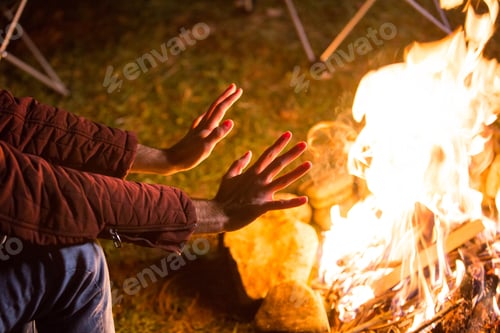 Preview: Young man warming up his hands over campfire