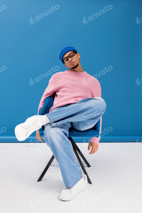 Preview: Handsome young man showcases trendy fashion style in playful pose against vibrant backdrop