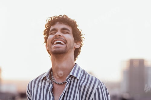 Preview: An attractive curly-haired guy in a striped shirt smiles against the backdrop