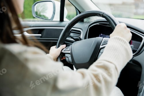 Preview: Young woman in a beige sweater driving a car.
