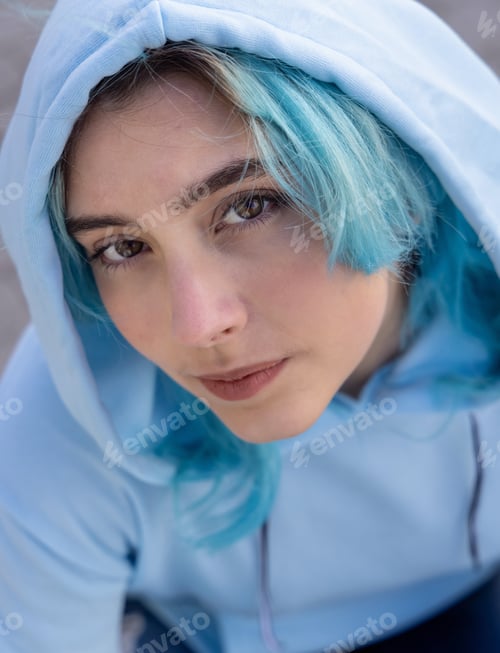 Preview: Blue haired Teenage girl in light blue oversize hoodie lookinginto a camera from down
