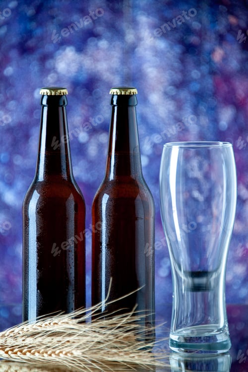 Vista previa: Vertical view of two full closed beer bottles and empty glass on blurred color background