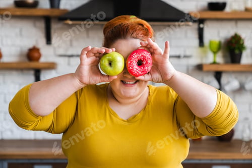 Preview: Corpulent fat plump caucasian woman holding apple and donut close to her eyes.