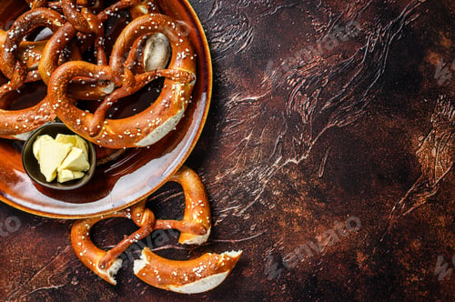 Preview: Freshly baked homemade pretzel with salt on a rustic plate. Dark background. Top view. Copy space