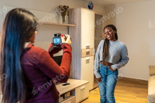 Preview: Young photographer taking pictures of her friend posing at home