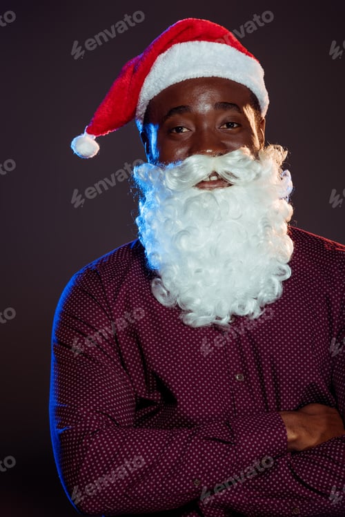 Preview: smiling african american man in santa hat and beard posing with crossed arms on black