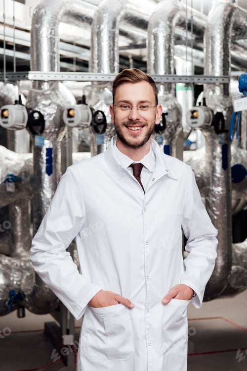 Preview: cheerful engineer in white coat standing with hands in pockets