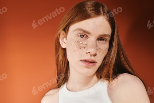 Preview: Young queer man with stylish red hair and freckles posing against a warm orange backdrop