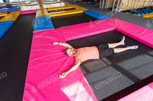 Preview: Fitness, fun, leisure and sport activity concept - Man lying on a trampoline indoors, top view