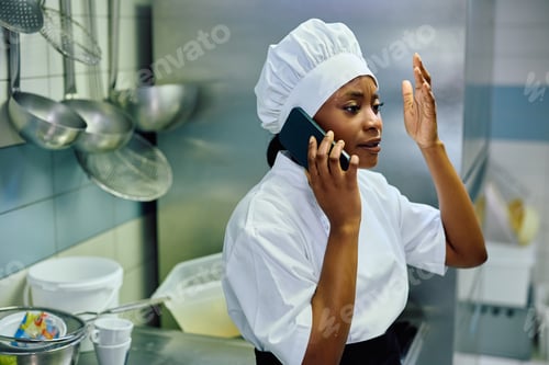 Preview: Professional black cook talking on her mobile phone while working in the kitchen.