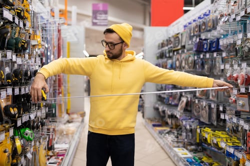 Preview: a young man chooses a construction roulette in a shop not for building goods