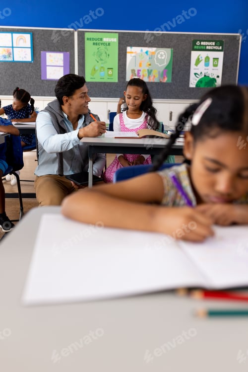 Preview: Diverse male teacher using tablet teaching children at desks in elementary school classroom