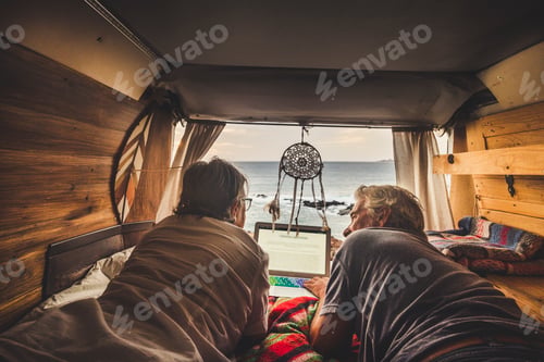 Preview: Senior couple traveling in a vintage van, using laptop