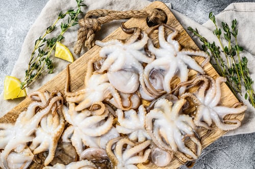 Preview: Raw baby octopus with thyme and lemon in a wooden bowl. Organic seafood. Gray background. Top view