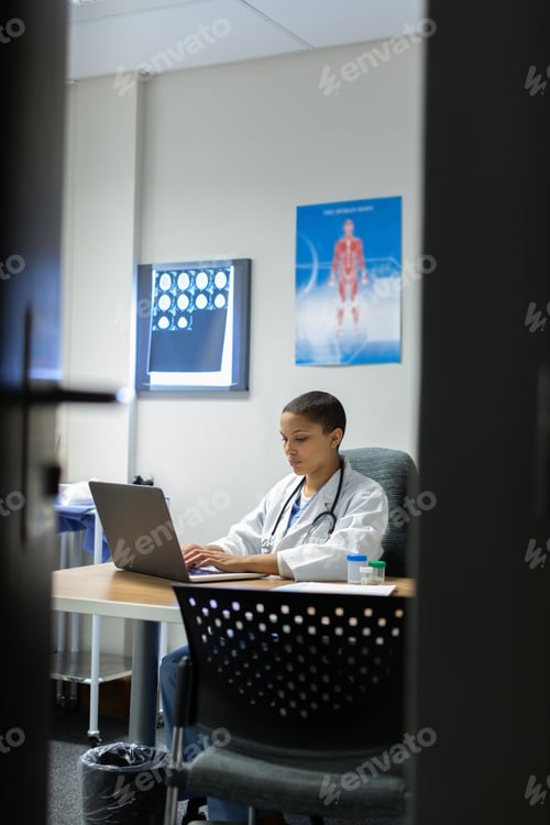 Preview: Front view of mixed-race female doctor working on laptop at desk of examination in hospital