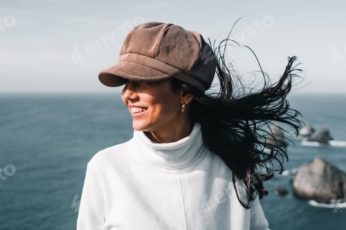 Preview: young caucasian woman in white sweater black hair and pretty corduroy hat with loose hair blown by