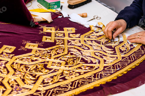 Preview: Holy Week textile manufacturing. Woman correcting embroidery pattern with gold thread.