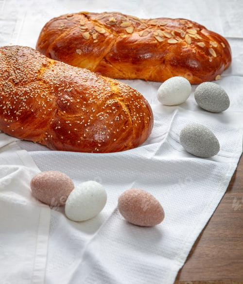 Preview: Easter sweet bread, two tsoureki braids and Easter eggs on white table cloth, closeup