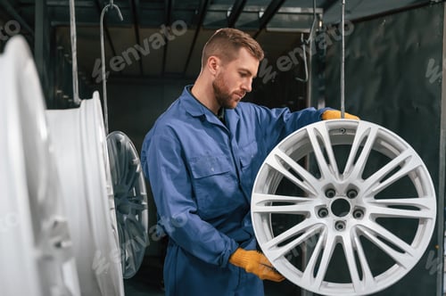 Preview: Disk of wheels are hanging. Car service station worker is indoors