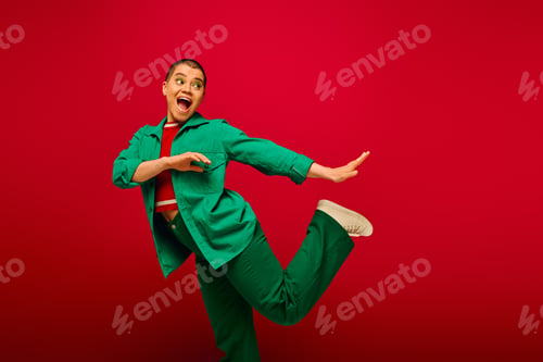 Preview: stylish look, bold makeup, amazed and tattooed, short haired woman in green outfit posing on red