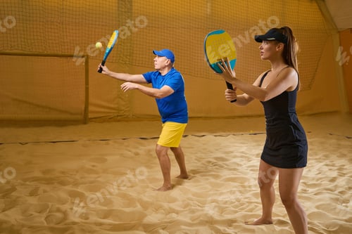 Preview: Woman with racket looks at man on sandy tennis court